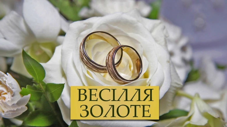 Золоті обручки на білій троянді для привітання з золотим весіллям.