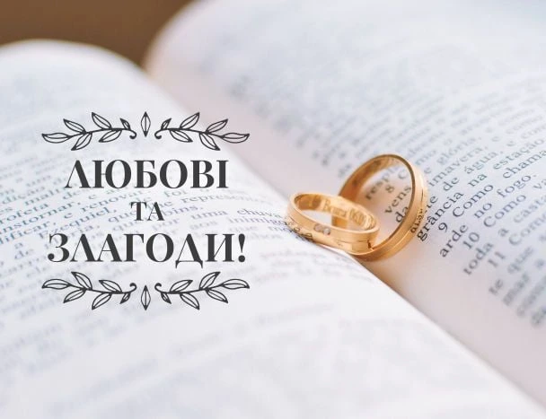 Золоті весільні кільця на відкритій книзі з привітанням українською.